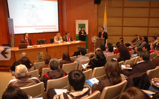 Se ve un auditorio con los asistentes de espaldas y 5 personas en el escenario