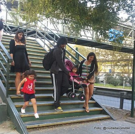 Una pareja baja un coche de niños por las escaleras de la pasarela peatonal del Parque Arauco