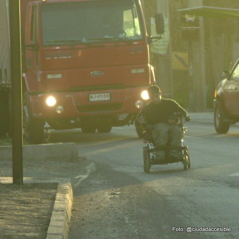persona en silla de ruedas circulando por la calzada delante de un camión