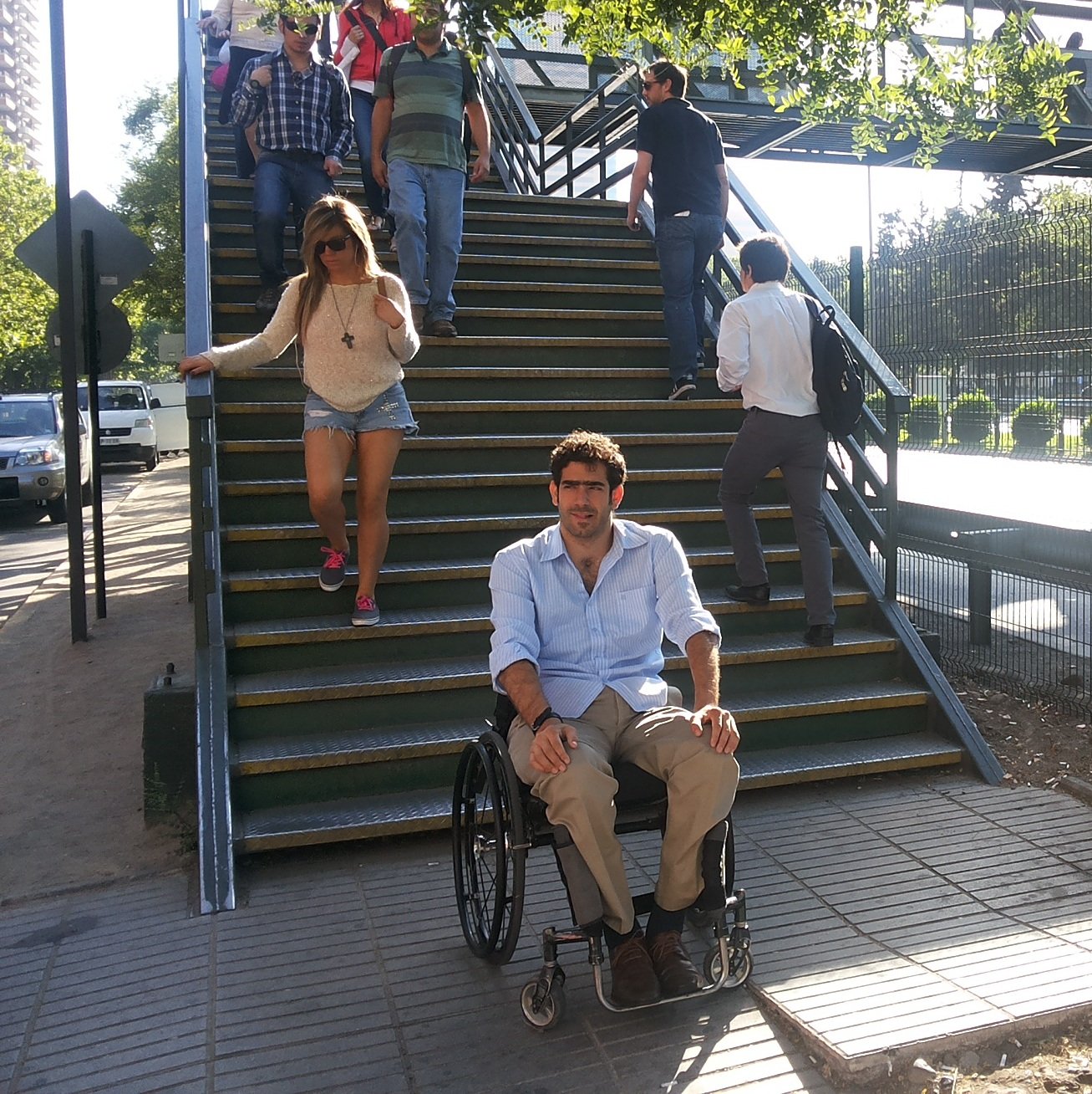 persona en silla de ruedas frente a escaleras de pasarela peatonal