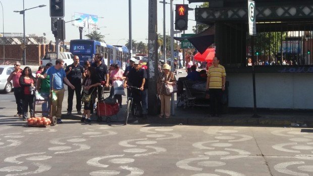 Cruce peatonal demarcado con figuras en Mapocho y varios peatones esperando cruzar