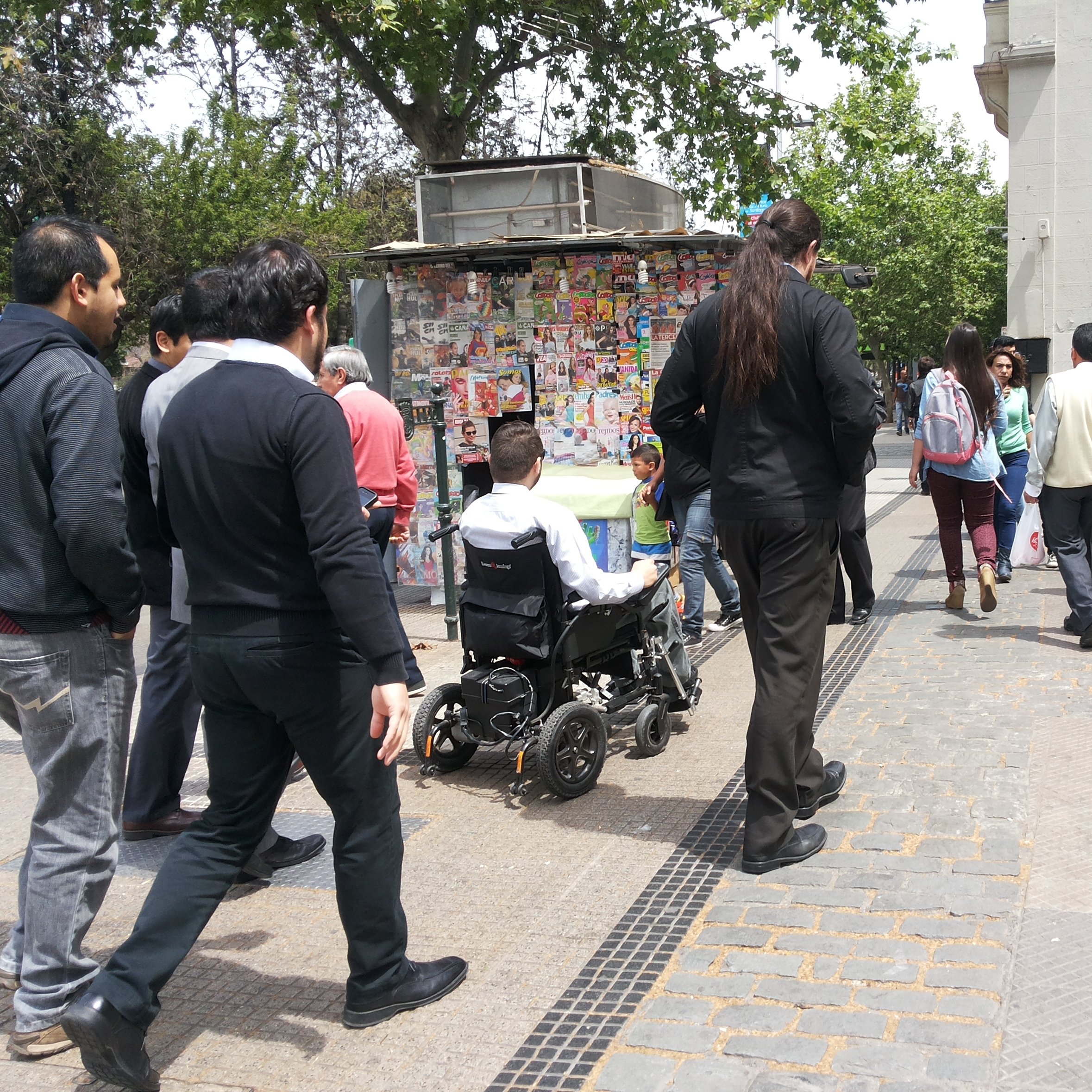 persona en silla de ruedas circulando frente a un puesto de revistas