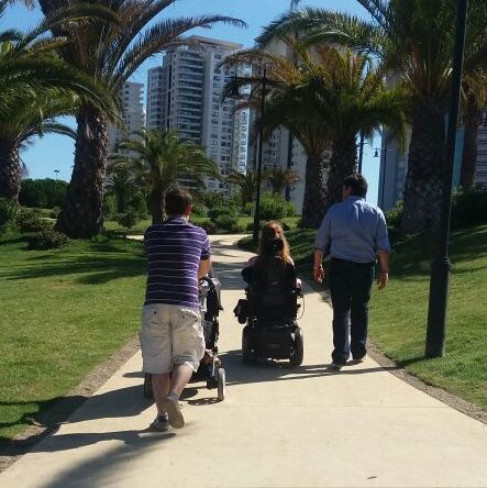 grupo de personas caminando por espacio publico una de ellas en silla de ruedas y otra llevando un coche de niños