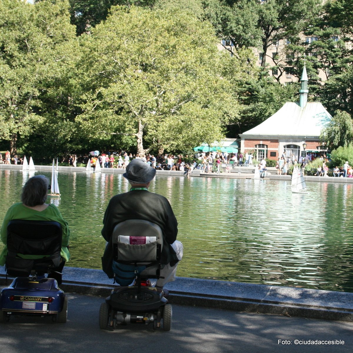 dos adultos mayores en sillas scooter mirando una laguna en parque