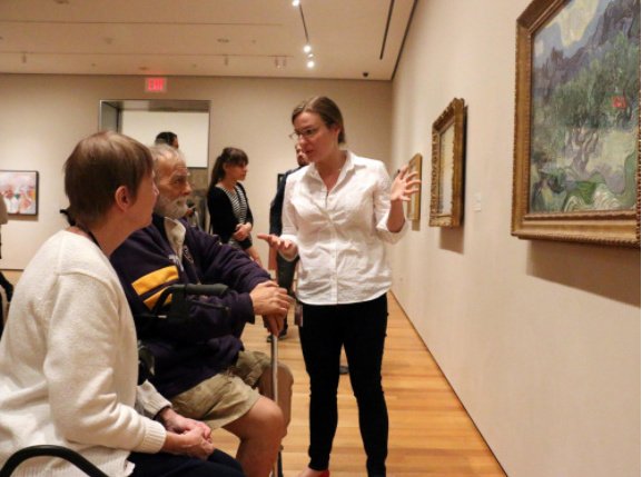 mujer describe un cuadro a apersonas con discapacidad en un museo