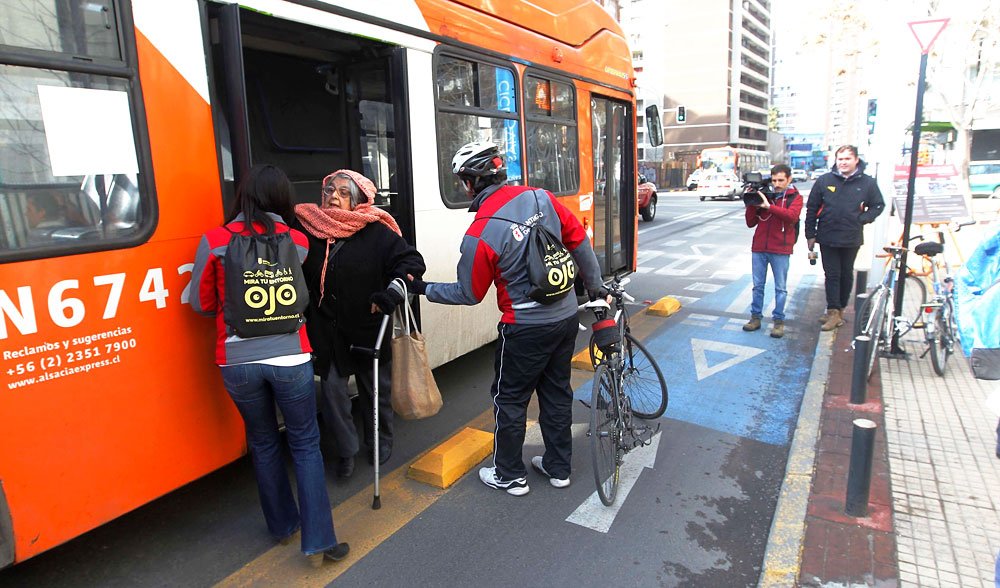 adulto mayor bajando con ayuda y dificultad de una micro en un espacio que corresponde a una ciclovía