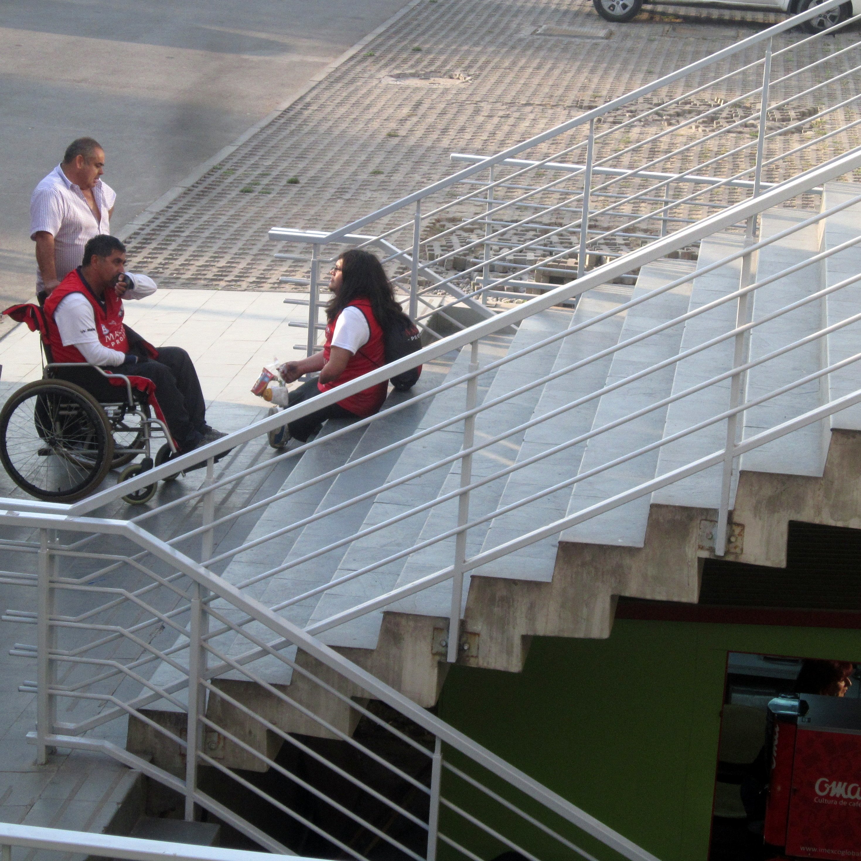 tres personas una en silla de ruedas esperan en el inicio de una escalera