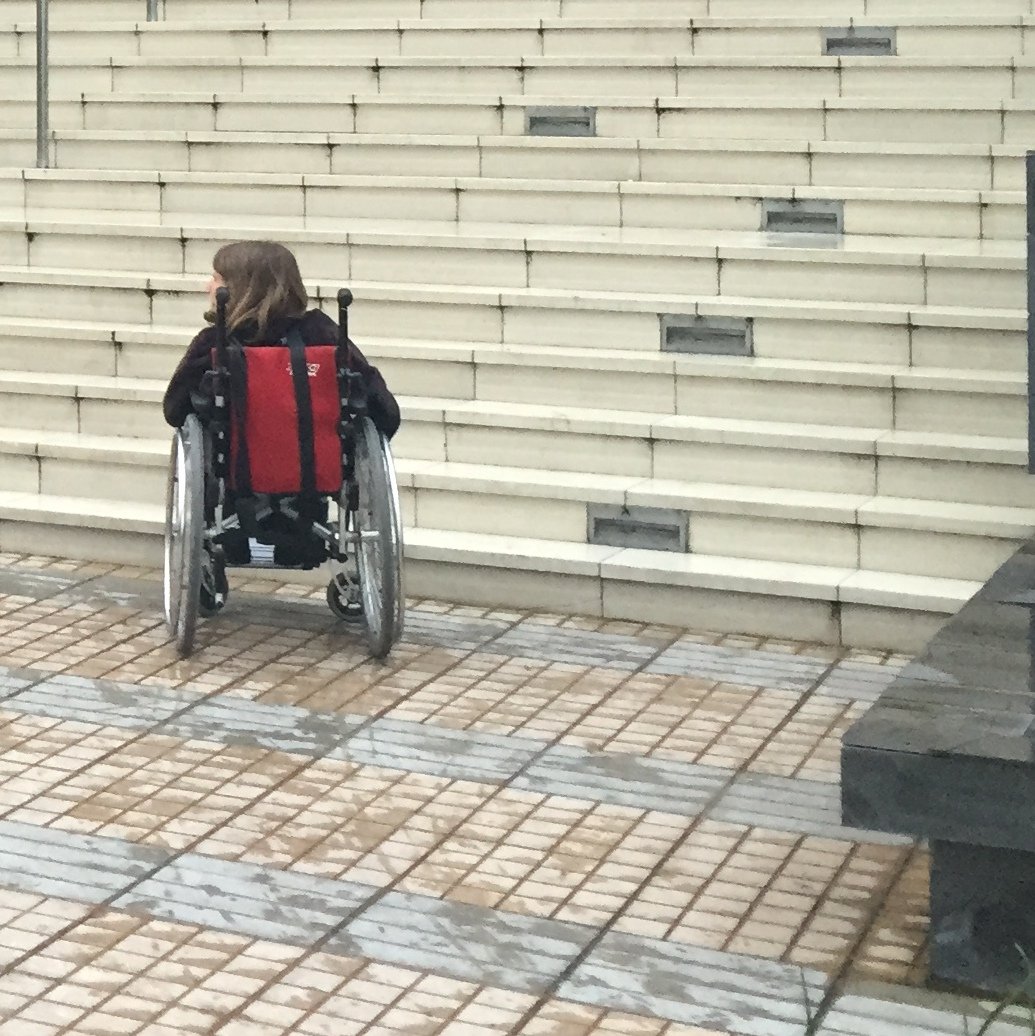 Joven en silla de ruedas enfrentando peldaños de una escalera