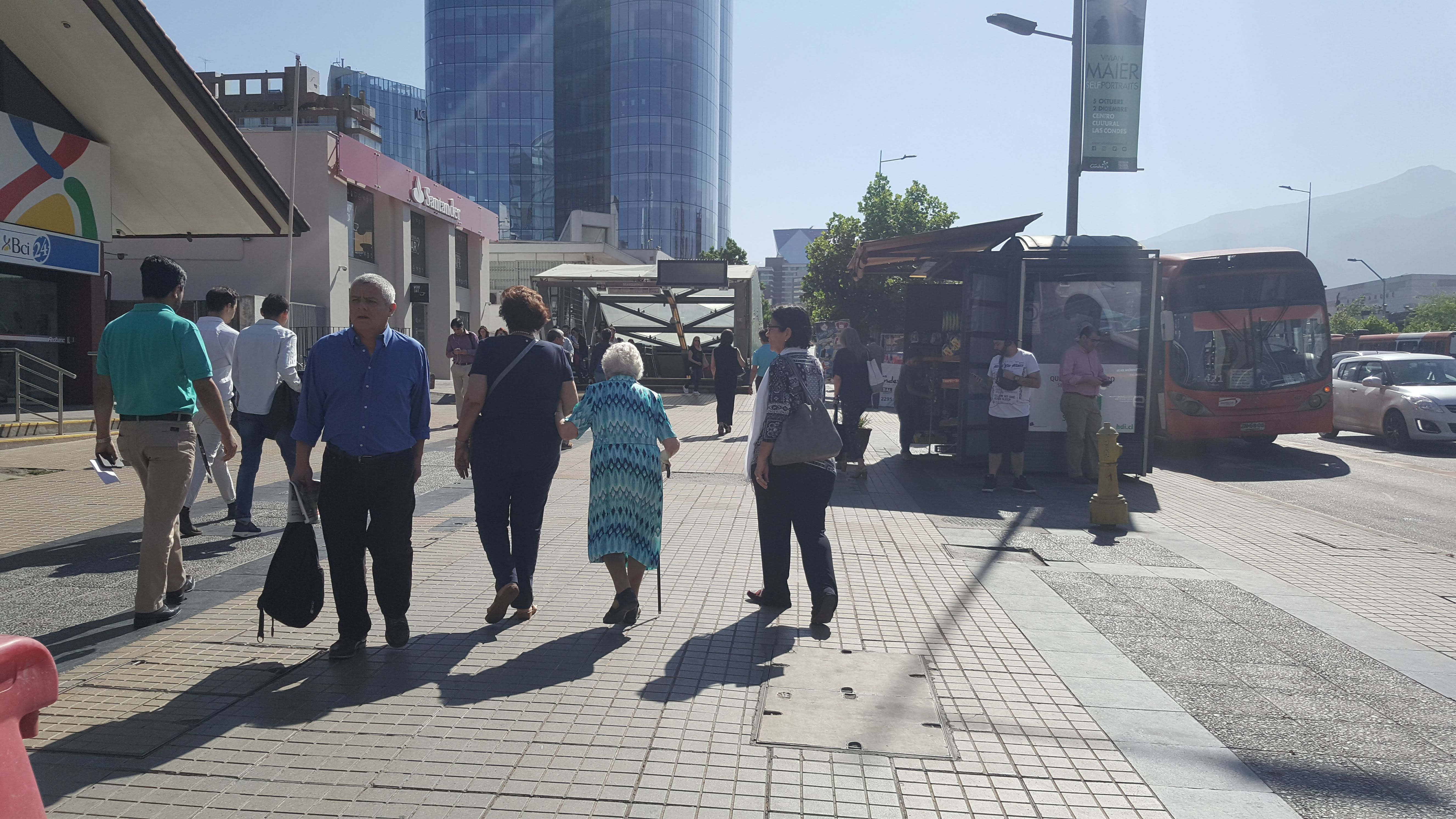 una persona adulta mayor y otros peatones por la vereda de calle apoquindo