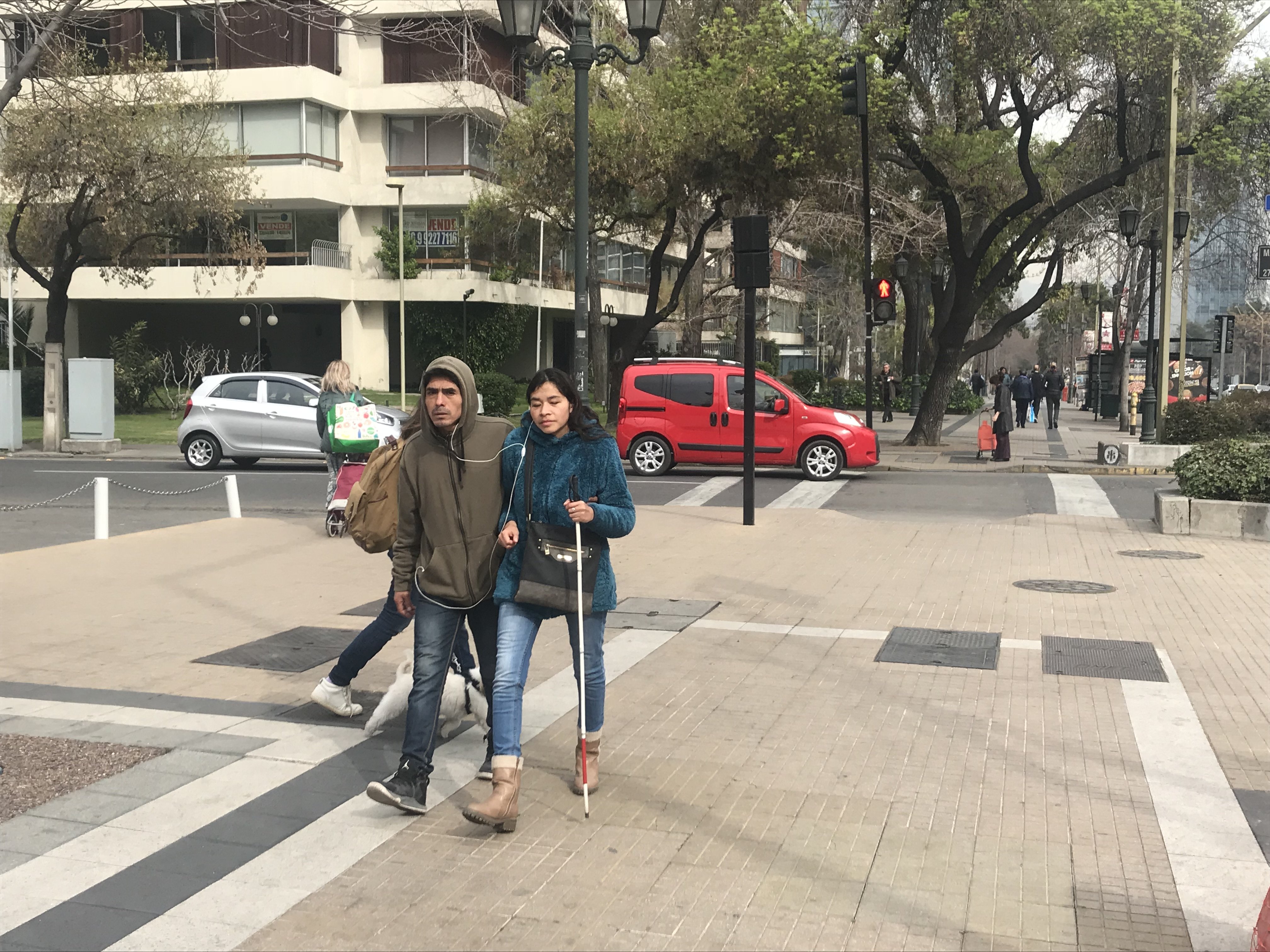 una persona ciega con acompañante circulando por una vereda de calle apoquindo