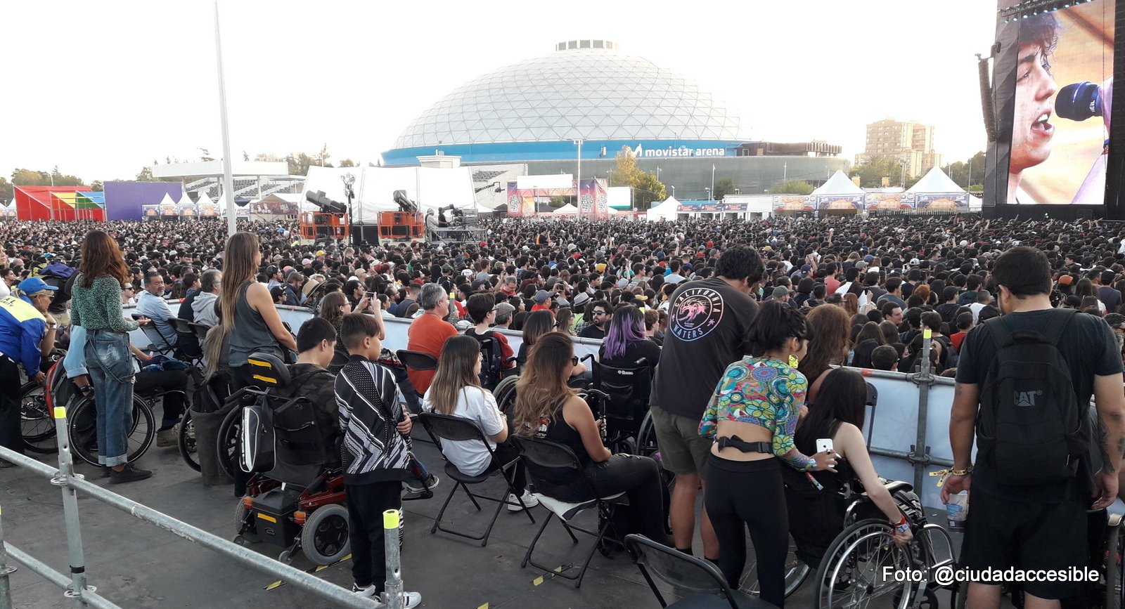 varias personas en silla de ruedas con sus acompañantes en sectores elevados para espectadores en silla de ruedas con vista al escenario