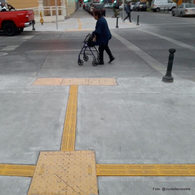 mujer con andador cruzando la calzada en una de las esquinas intervenidas con pavimento podotactil en Iquique