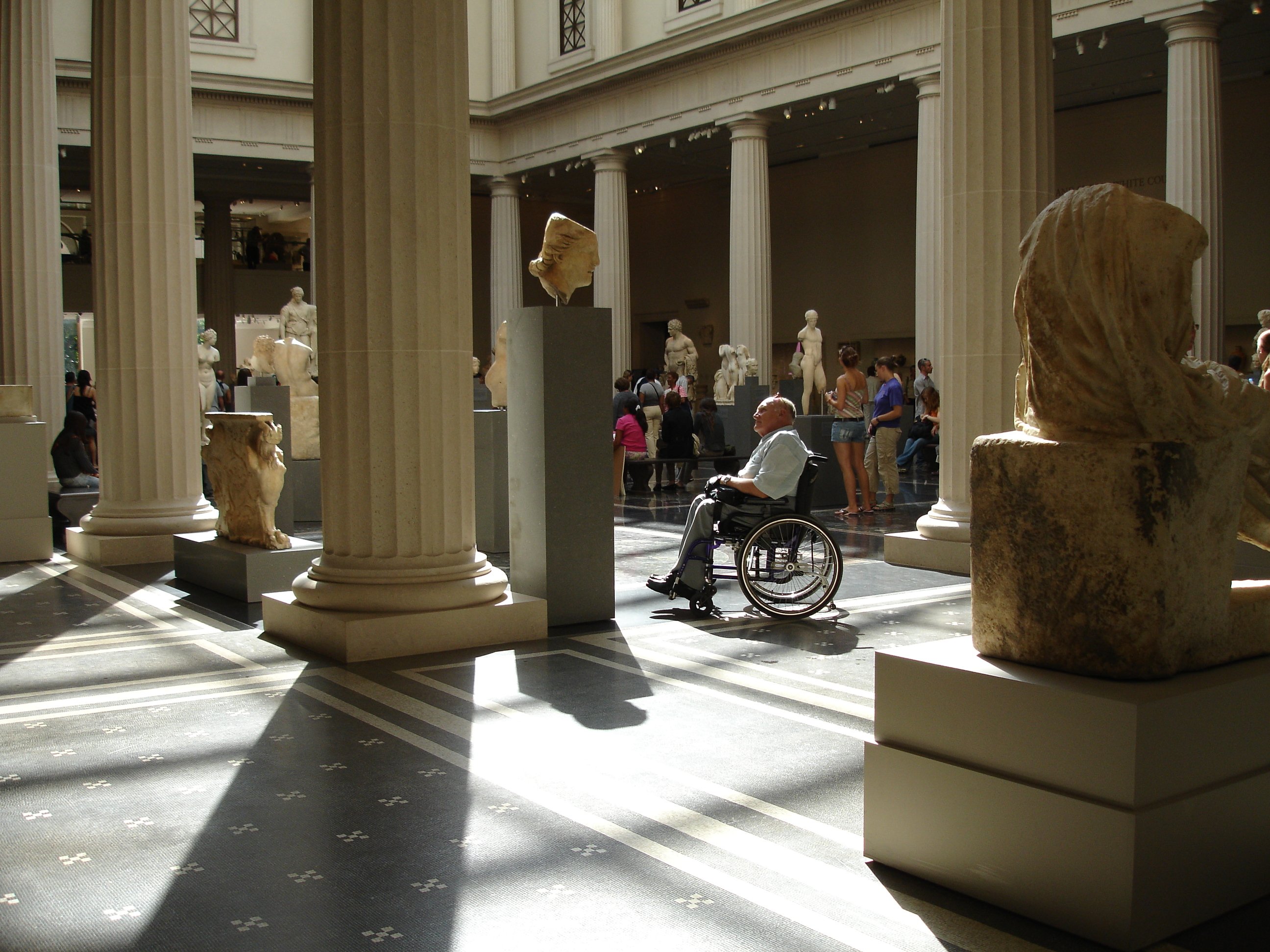 adulto mayor en silla de ruedas observando una escultura en un museo