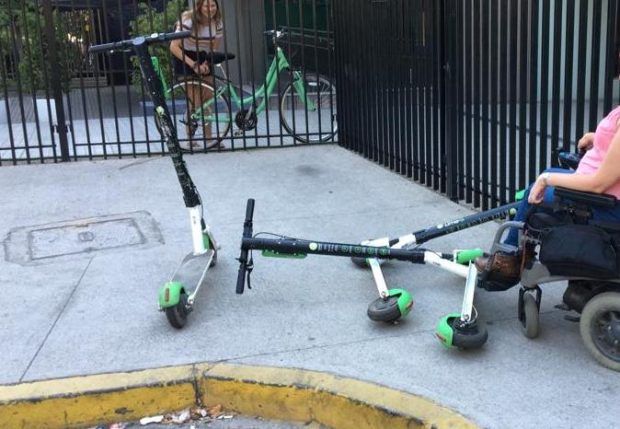 Mujer en silla de ruedas enfrentando tres scooter tirados sobre la vereda
