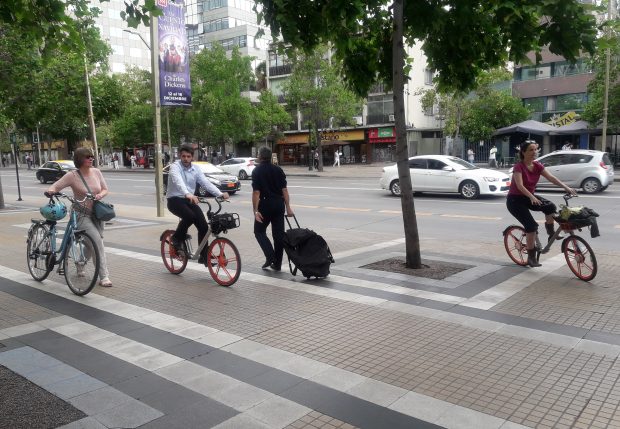 tres ciclistas sobre una vereda donde una de ellas va caminando y llevando la bicicleta