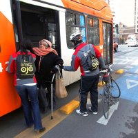 adulto mayor bajando con ayuda y dificultad de una micro en un espacio que corresponde a una ciclovía