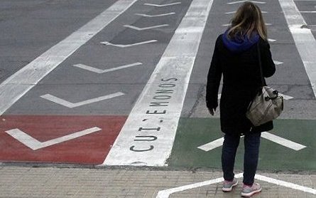 mujer espera cruzar una calle demarcada con señales para encauzar a los peatones hacia uno u otro sentido