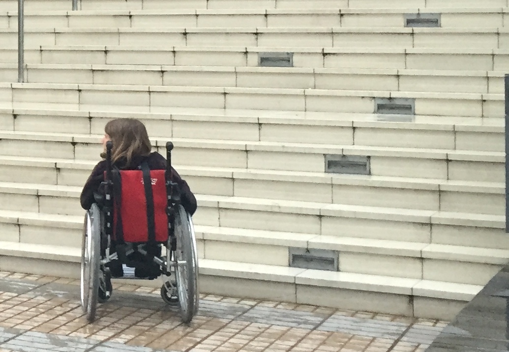 joven en silla de ruedas frente a numerosos peldaños de una escalera