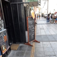 un letrero promocionando comida está instalado sobre la franja podotáctil de avance