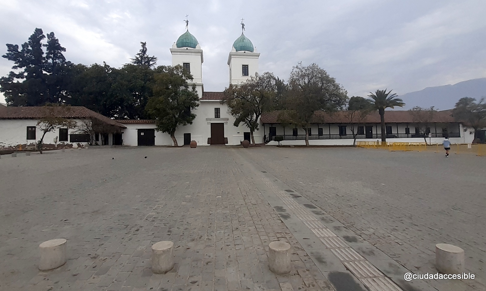 vista hacia la iglesia donde se ve una línea de bolardos grises de baja altura en medio de pavimento de adoquín