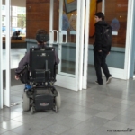 dos personas una en silla de ruedas acceden a un edificio a través de unas puertas