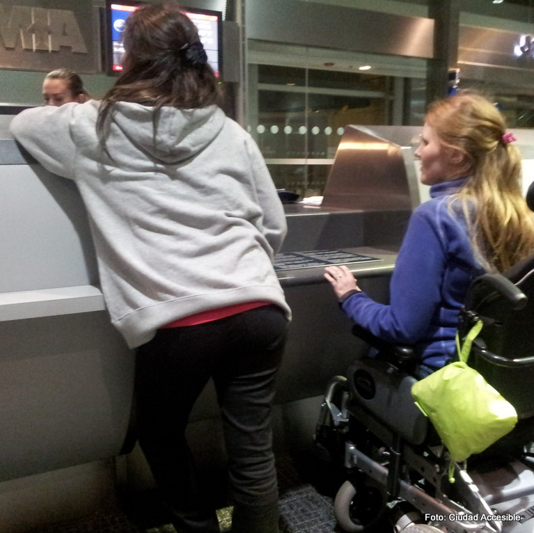Foto de dos personas, una de ellas en silla de ruedas frente a un mostrador de atención