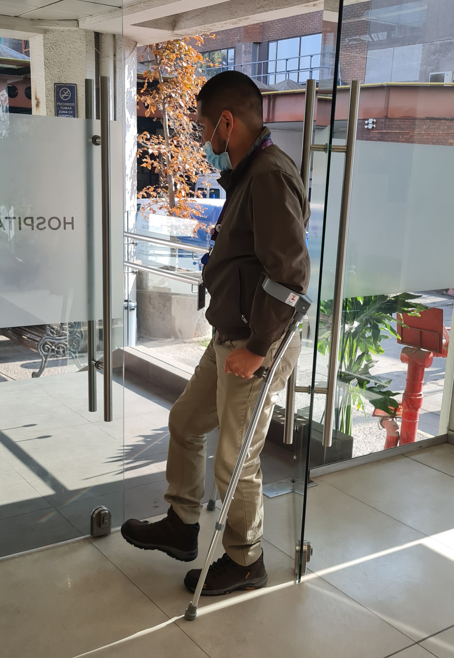 Un hombre intenta abrir una pesada puerta de vidrio usando bastones de apoyo en ambas manos