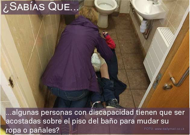 Foto de una mujer mudando a un niño mayor en el piso de un baño público.