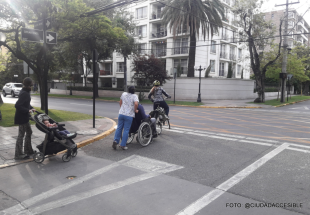 una persona llevando un coche otra empujando una silla de ruedas y un ciclcista esperando cruzar una calle