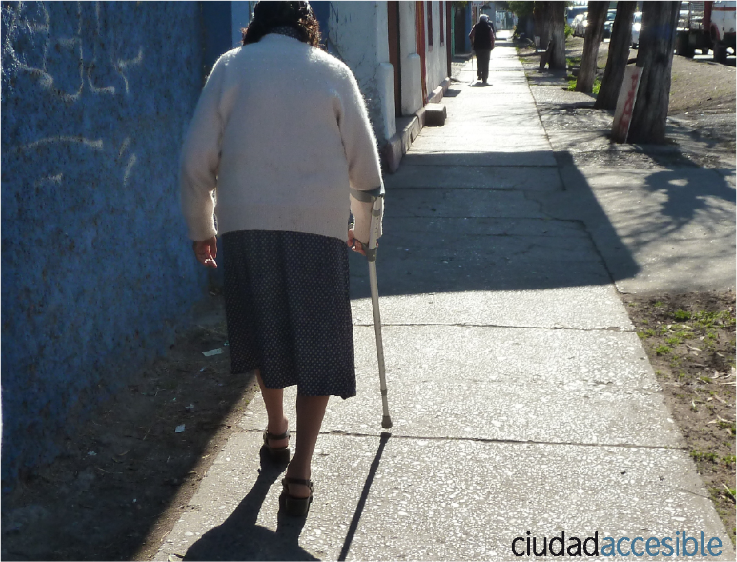 vista de espaldas de una mujer mayor camina por una vereda apoyada en un bastón