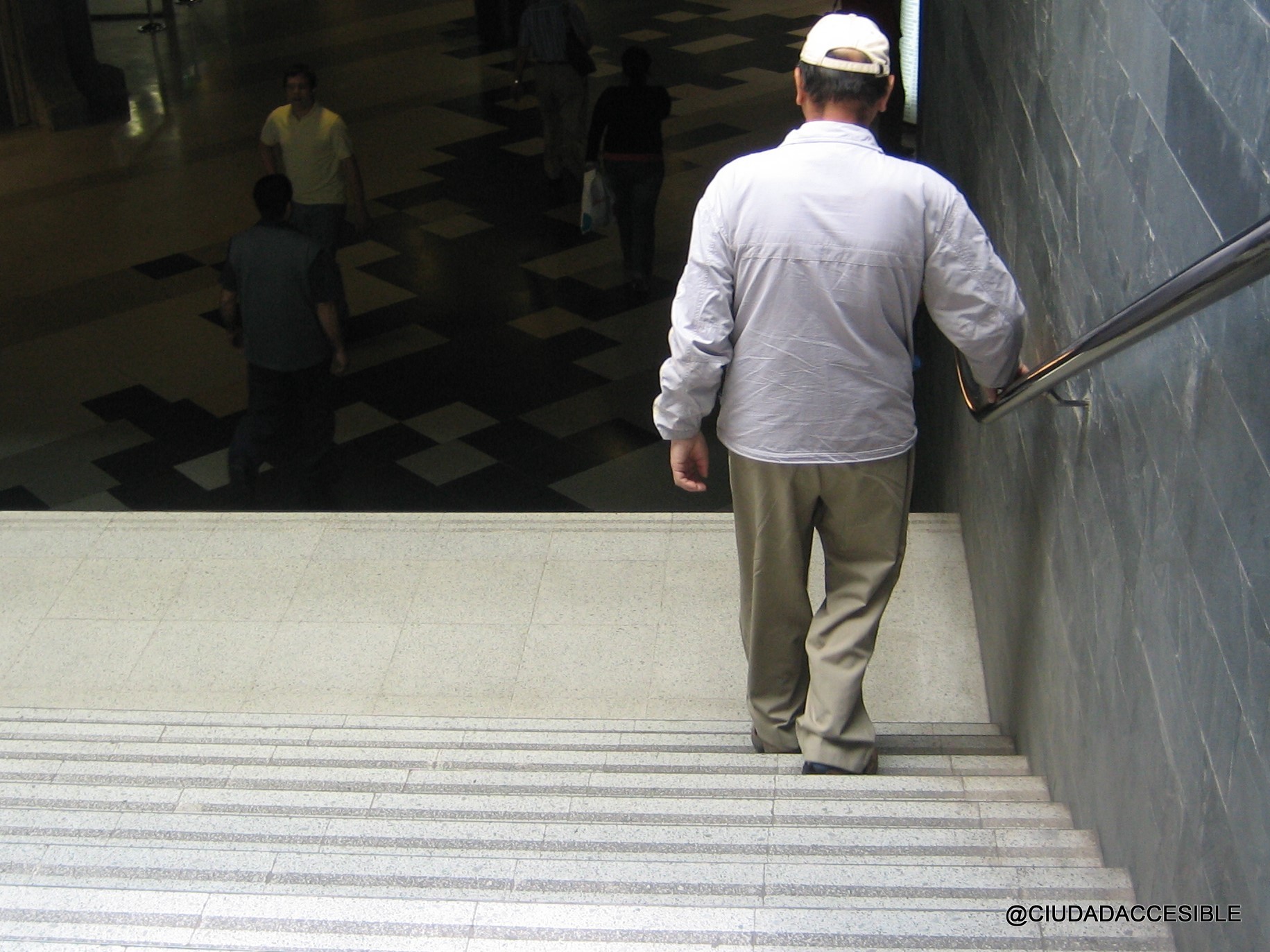 persona mayor baja una escalera apoyándose en un pasamanos