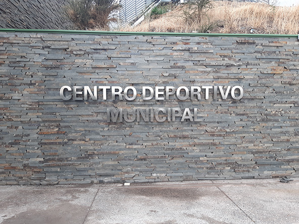 Se ve una pared de piedra con letras en acero donde se lee centro deportivo municipal