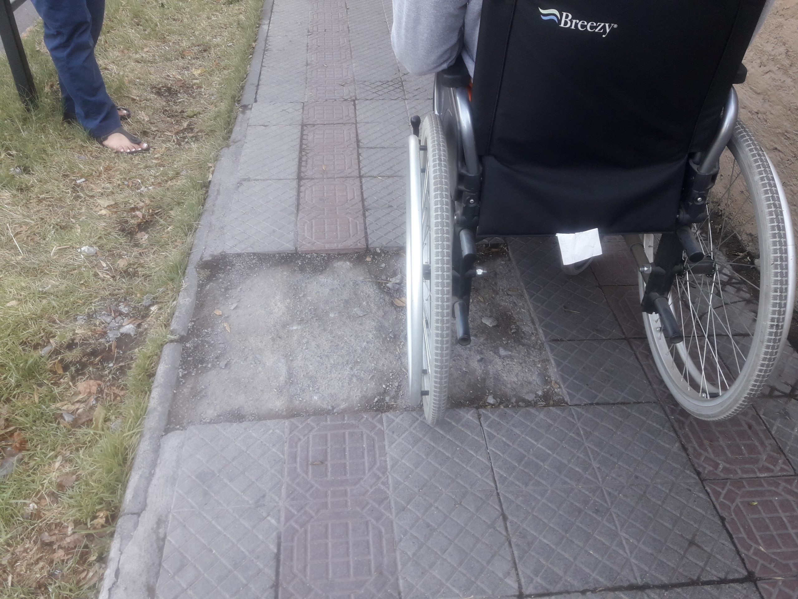 silla de ruedas circula por una vereda a la que le faltan varias baldosas