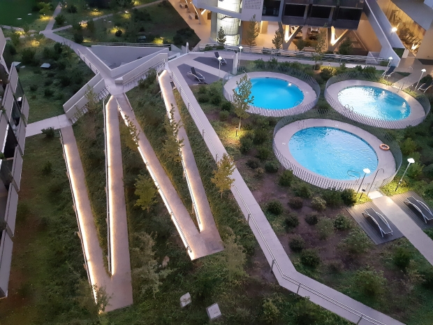 Se ve una larga rampa en zig zag que comunica a través de jardines en pendiente el área de piscina con el edificio.